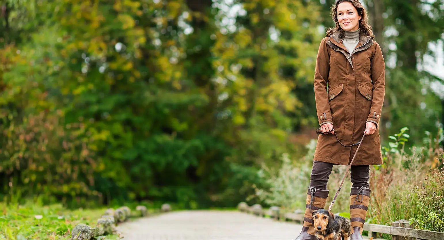 Woman in a brown leather coat on a path with a dog, showcasing a Baleno Chelsea Waterproof Coat.