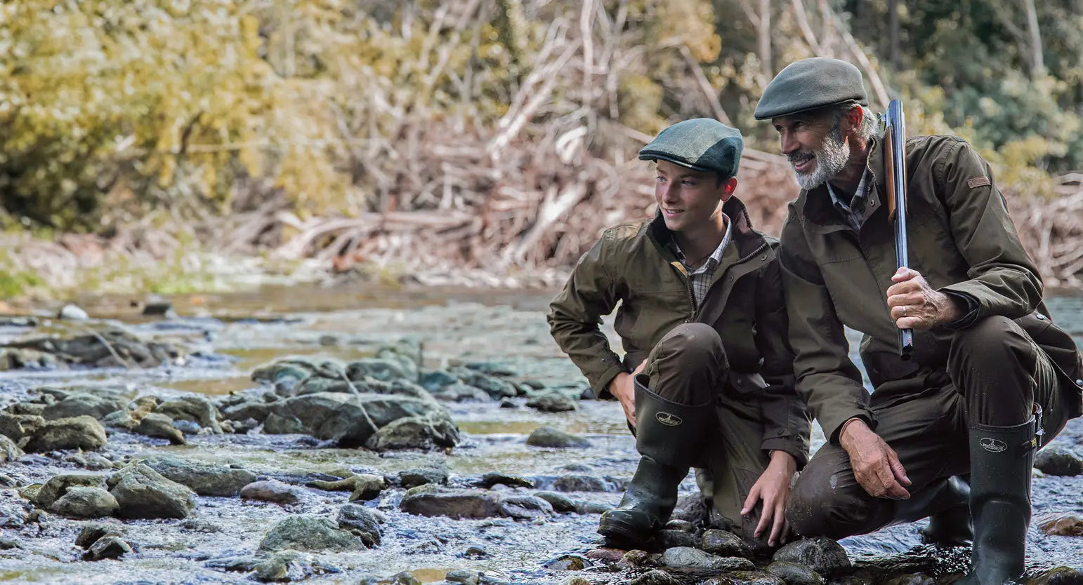 Two men in forest clothing fishing by a stream for Father’s Day adventure.