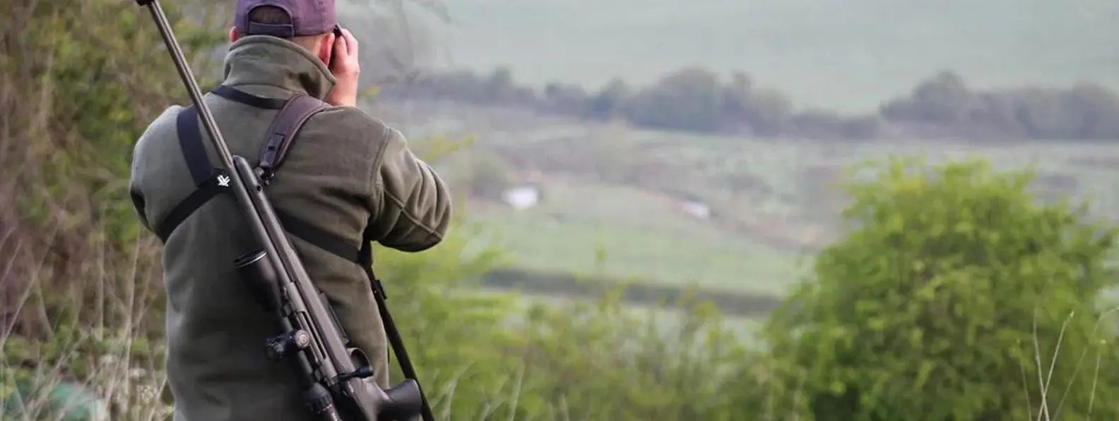 Hunter carrying rifle over shoulder scanning landscape in Hampshire Countryman article.