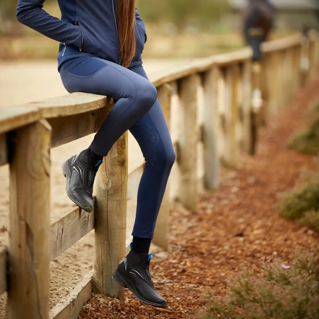 Person’s legs resting on a wooden railing in Ariat Boreas Half Grip Tight for outdoor adventures