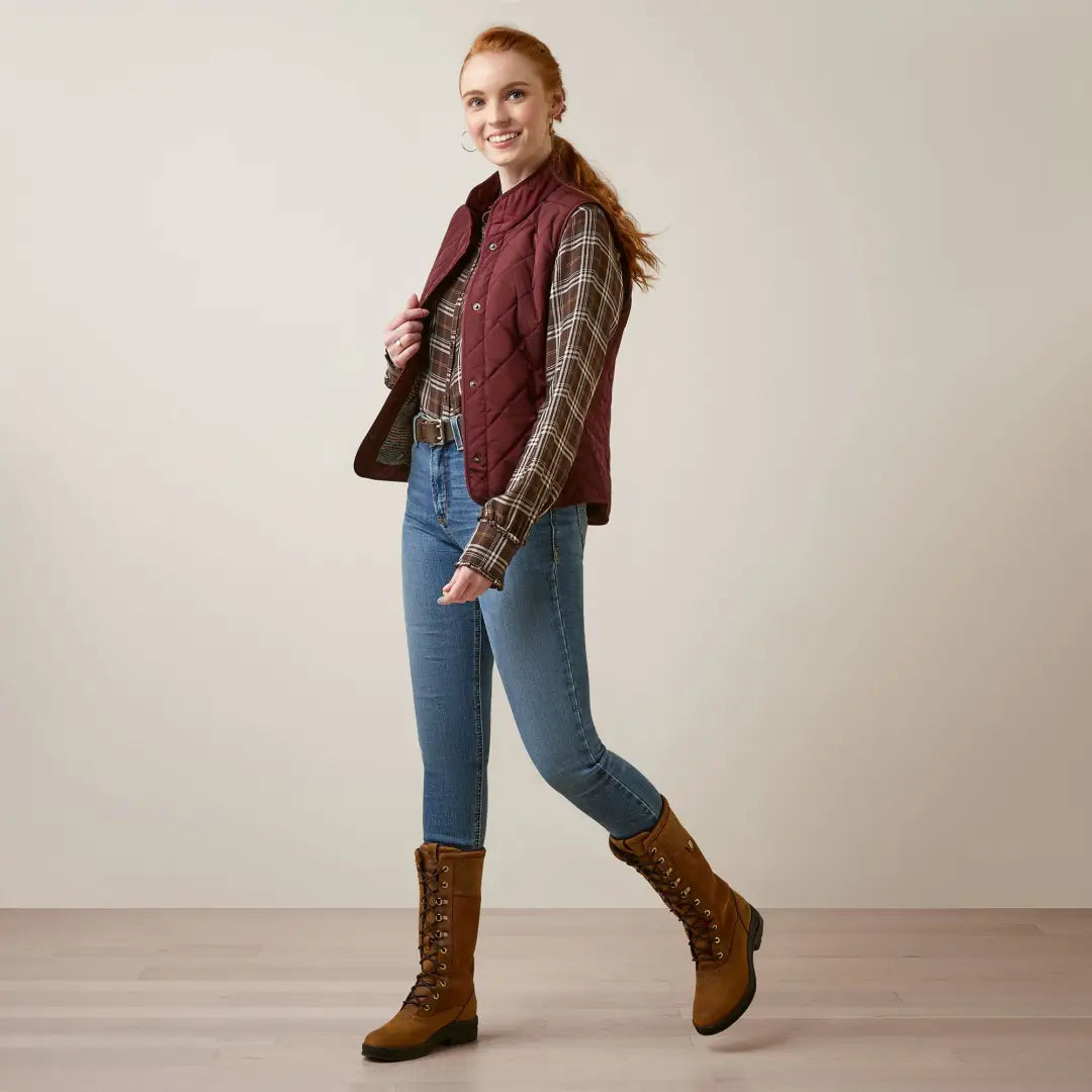 Woman in a burgundy Woodside Vest, stylish patterned sweater, jeans, and brown boots