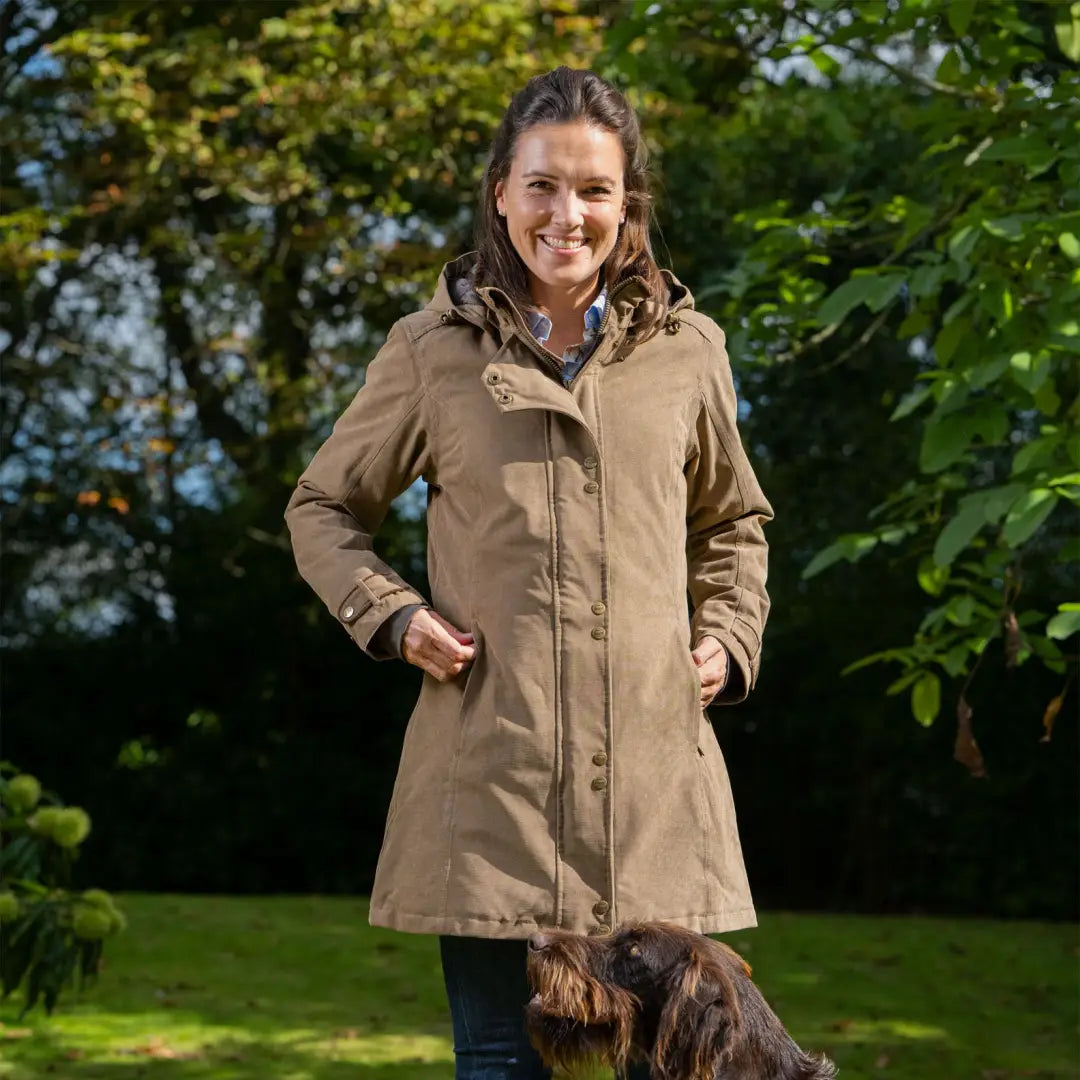 Smiling person in a tan Baleno Brooklands Waterproof Coat with a dog outdoors, warm ladies town look