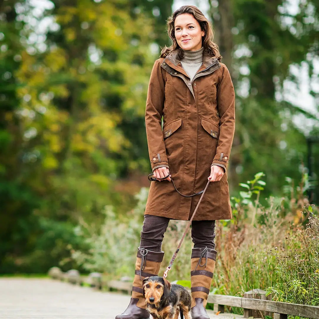 Woman in a brown Chelsea waterproof coat walking a small dog on a leash