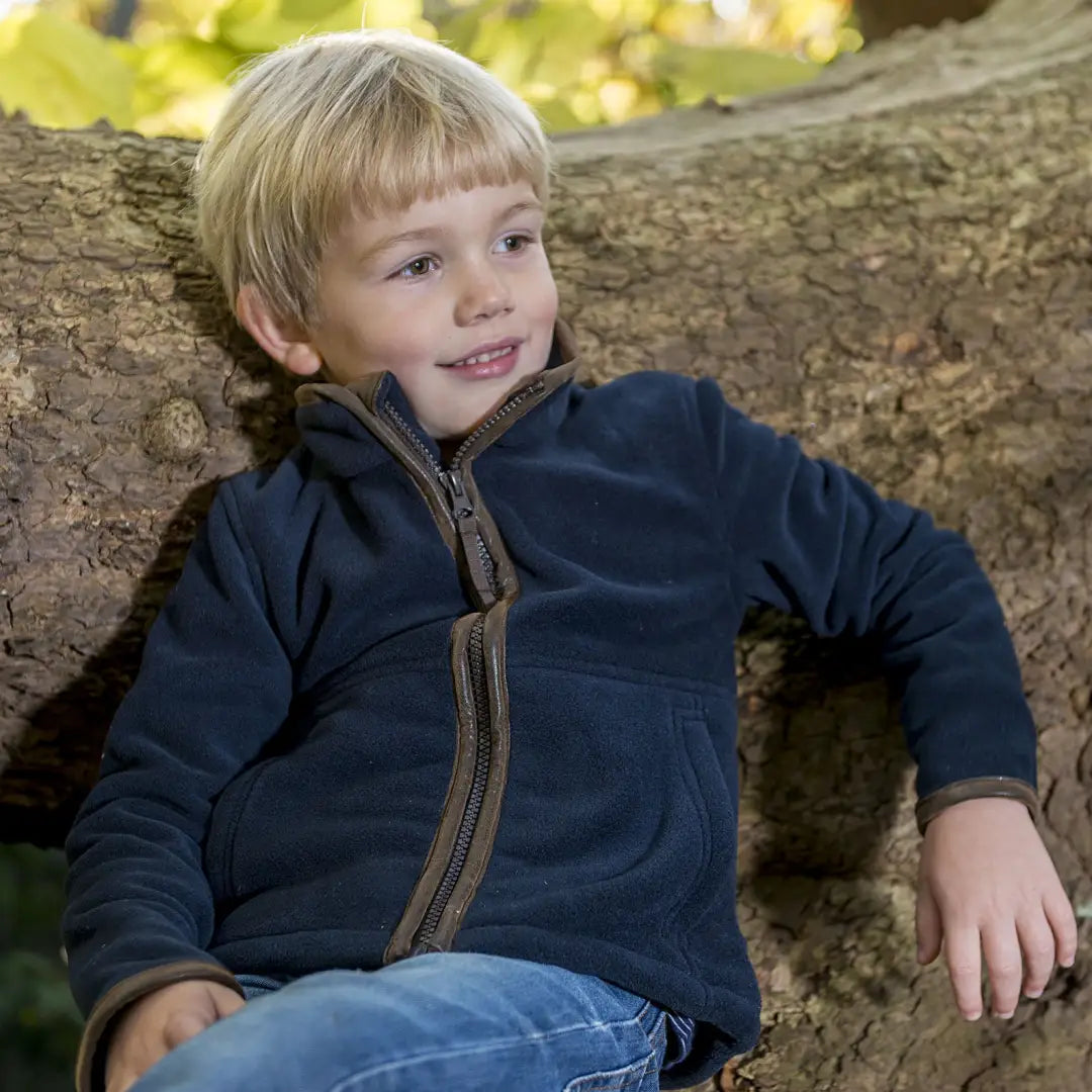 Young boy in navy blue sitting by a tree wearing a Baleno Cody fleece jacket