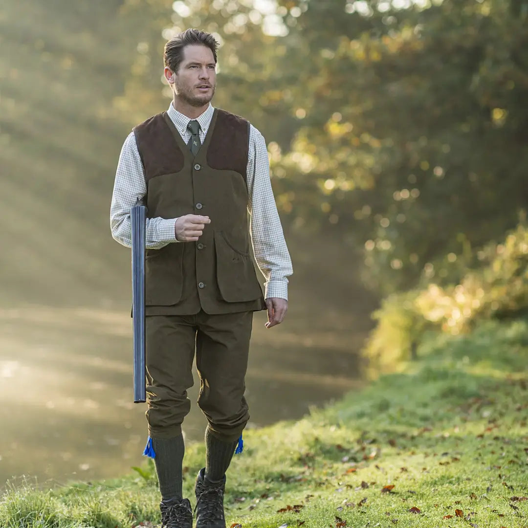 Man in countryside attire with shotgun showcasing Baleno Dolman traditional gilet