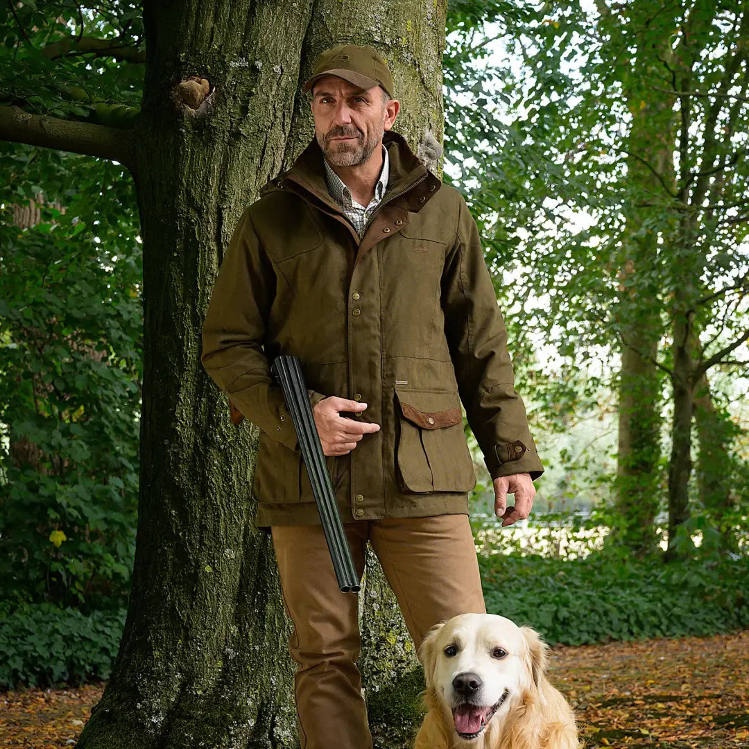 Man in Baleno Oakwood Waterproof Jacket by a tree with a shotgun and golden retriever