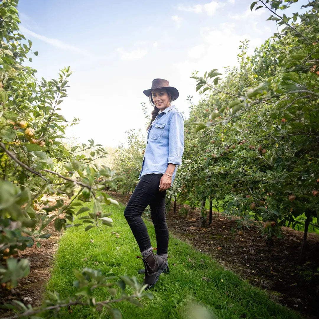 Woman in a blue shirt and hat enjoying the orchard with a stylish oiled leather hat