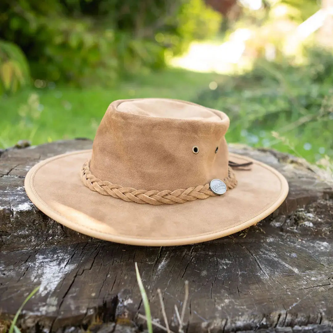 Tan Barmah Squashy Suede Leather Hat on a tree stump with a braided band