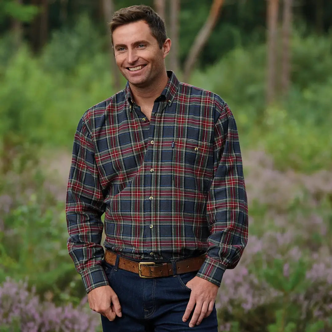 Smiling man in plaid flannel long sleeved shirt and jeans outdoors, wearing Champion style