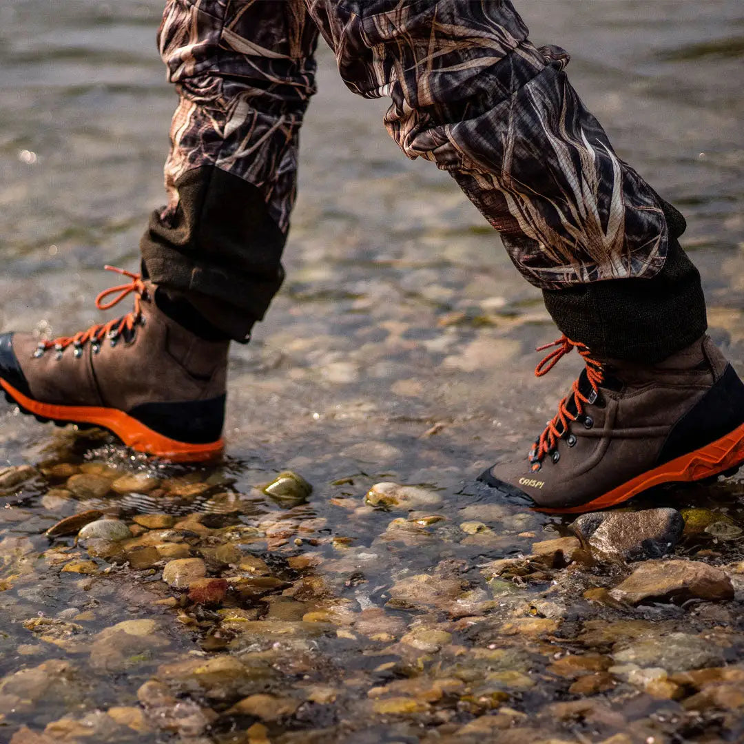 Crispi Valdres S.E. GTX boots with orange laces standing in water on rocky terrain