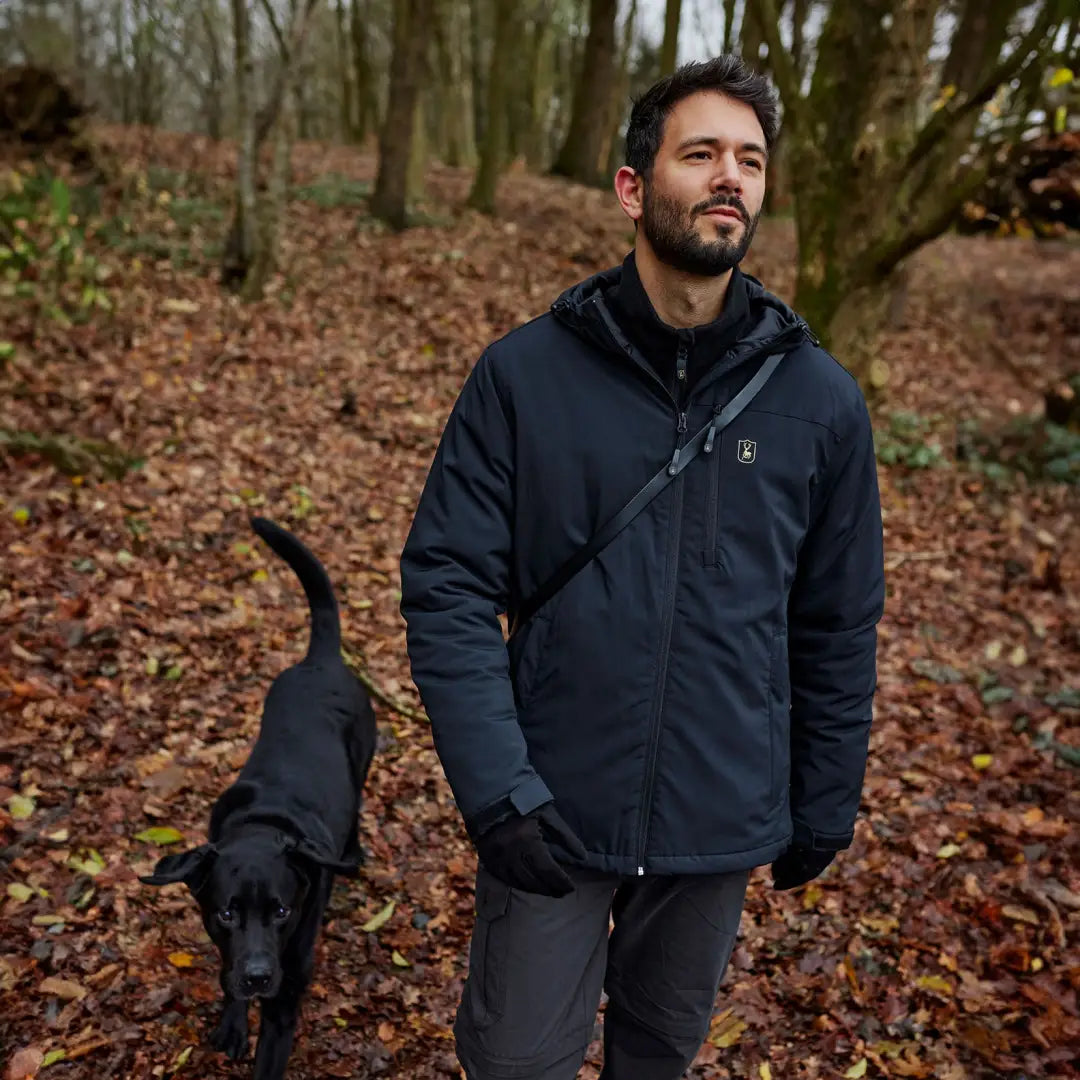 Man in a dark jacket with a black dog in the forest, promoting Deerhunter Denver Winter