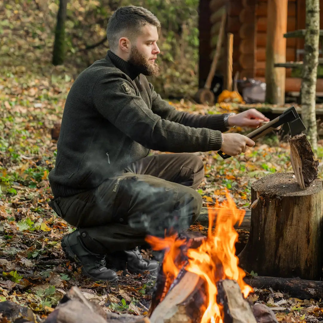 Man chopping wood by a campfire in Eagle Winter Trousers, perfect for winter adventures