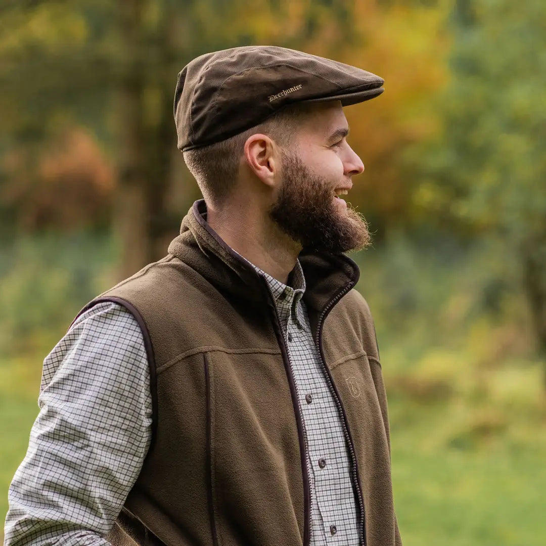 Bearded man in a flat cap and brown vest showcasing stylish country clothing for hunting