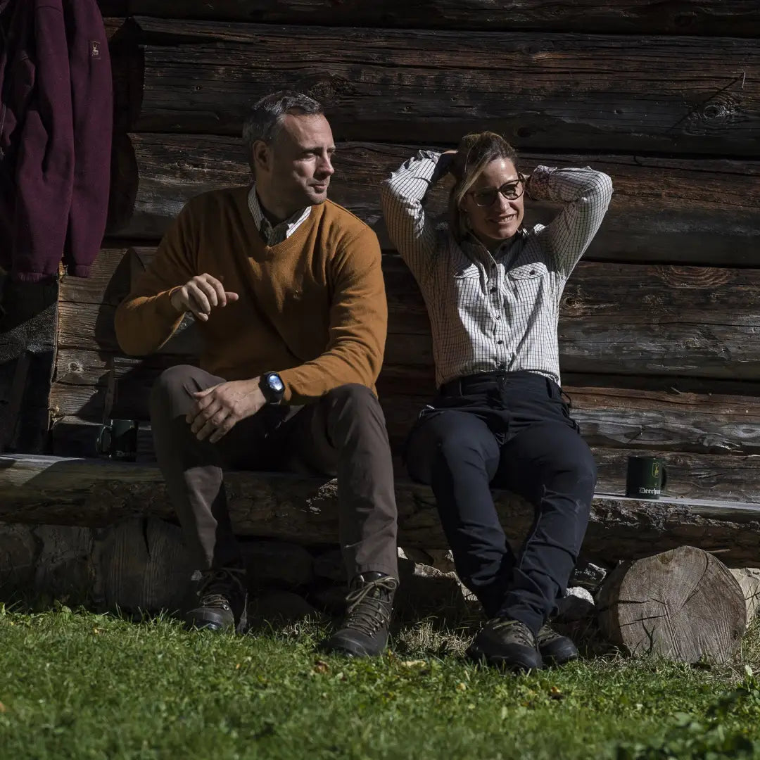 Two people on a bench by a log cabin wearing Deerhunter Lady Ann Full Stretch Trousers