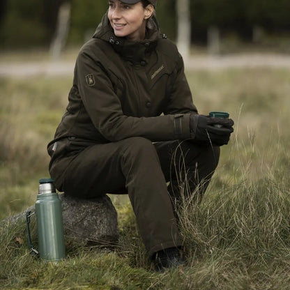 Woman in Deerhunter Lady Mary Trousers sits on a rock in a grassy outdoor spot