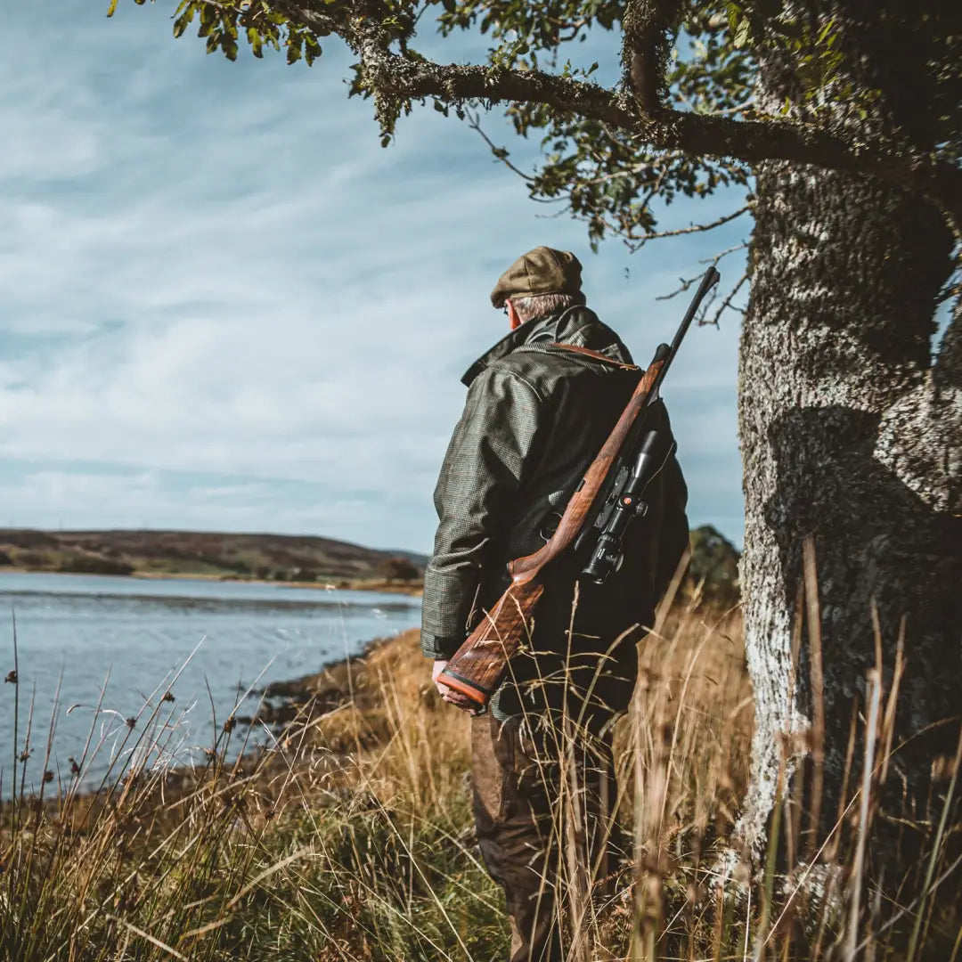 Hunter with rifle in Deerhunter PRO Gamekeeper Smock by water, featuring waterproof zipper