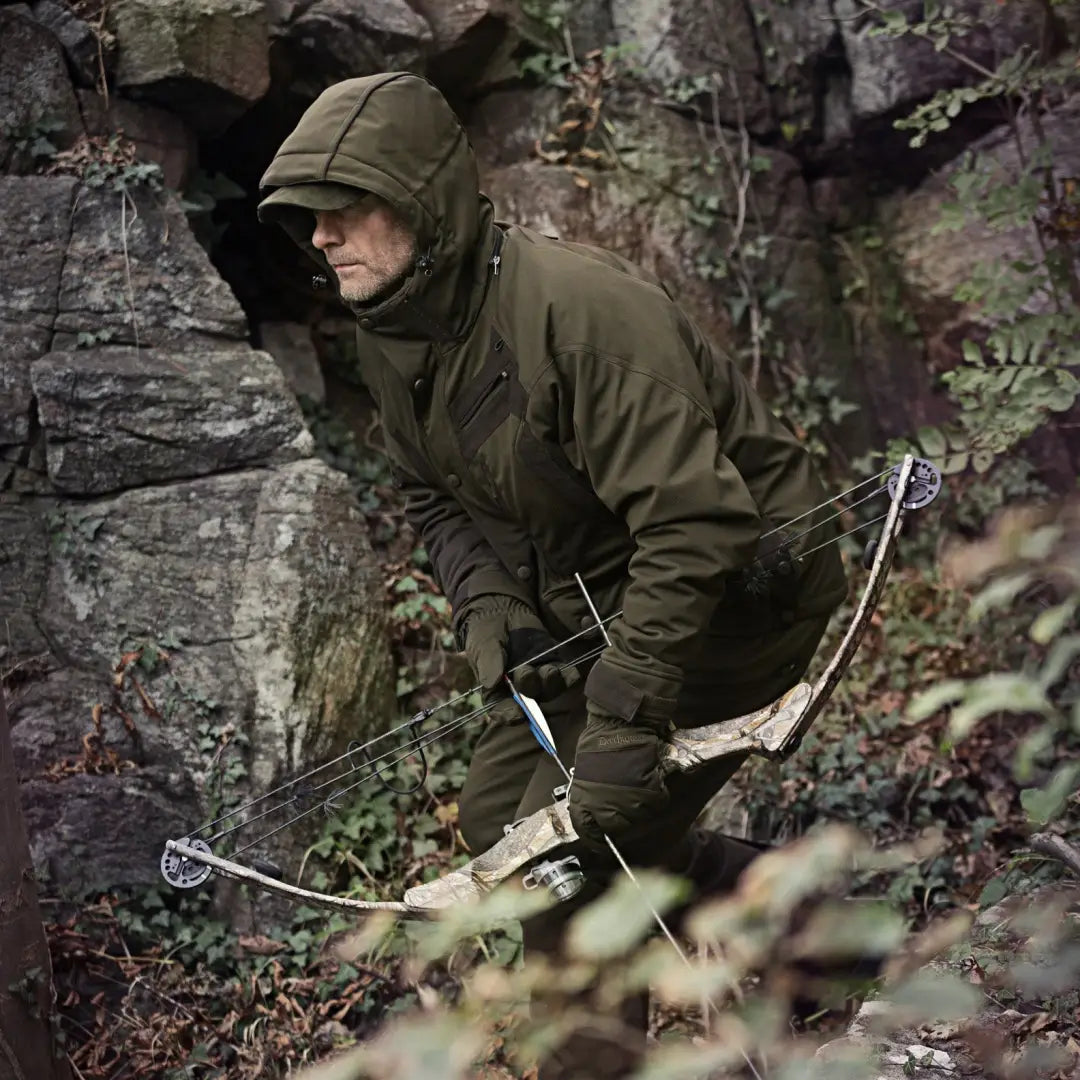 Person in camouflage with a crossbow wearing a Deerhunter Muflon Long Jacket in the forest