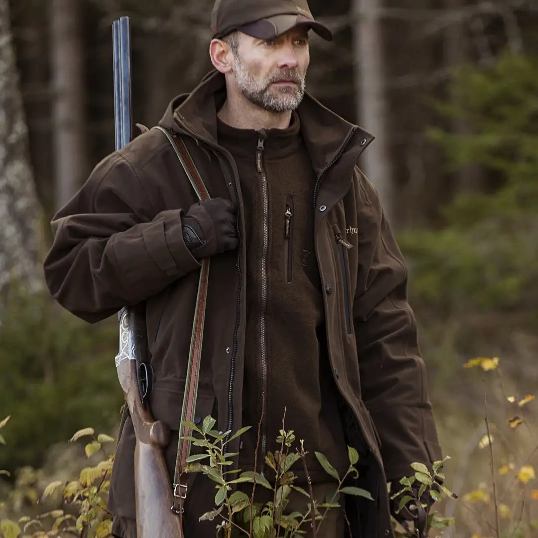 Bearded man in brown Deerhunter Pro Gamekeeper Jacket with rifle outdoors showcasing Deer-Tex® performance