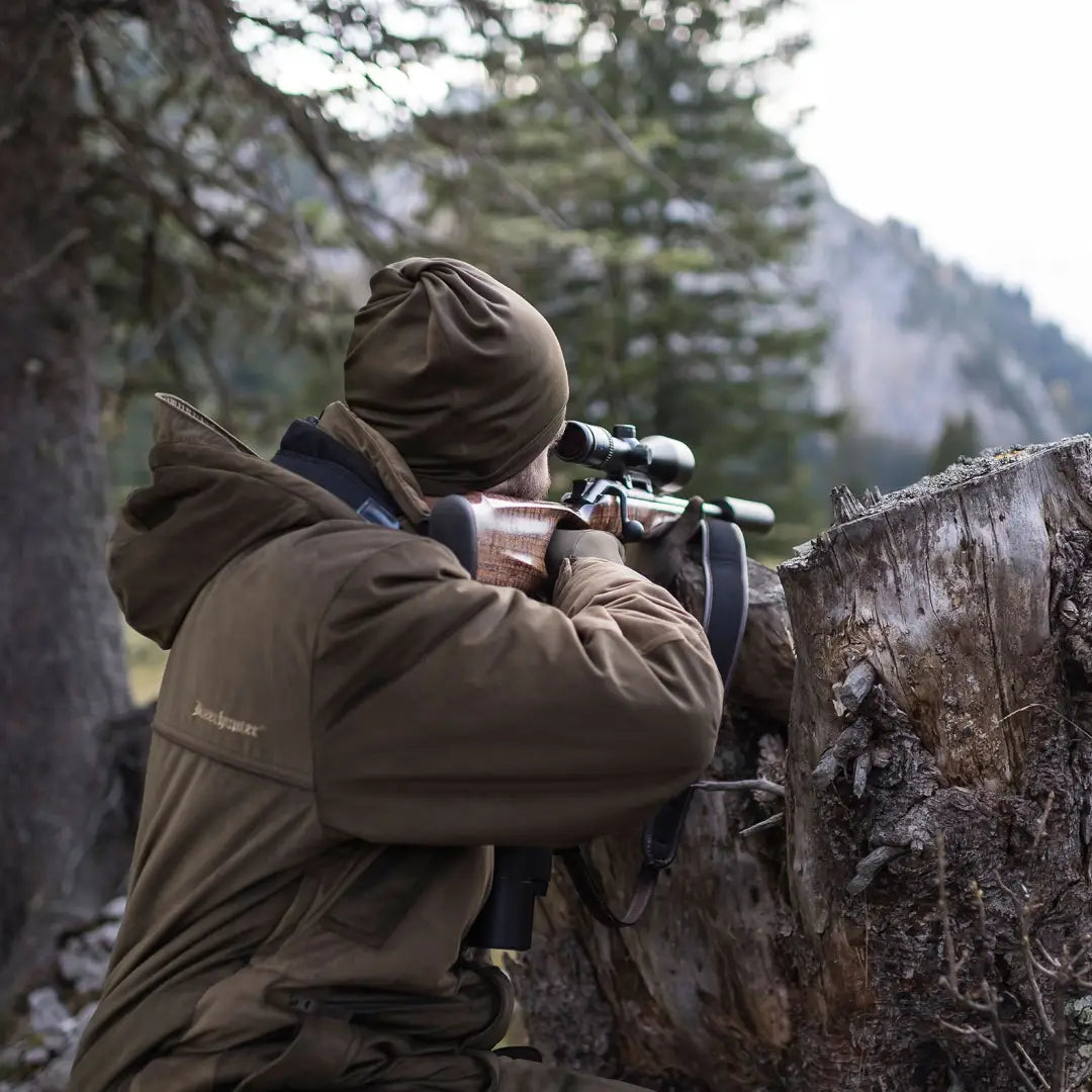 Person in hunting gear aiming a rifle with a scope while wearing a Rusky Silent Neck Tube