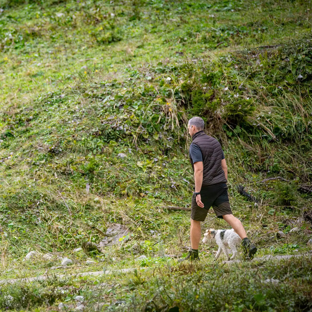 Person wearing Deerhunter Strike Shorts walking a dog on a sunny grassy hillside