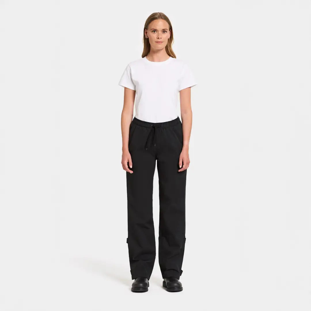 Woman in a white t-shirt and black pants showcasing Didriksons Grit functional rain pants