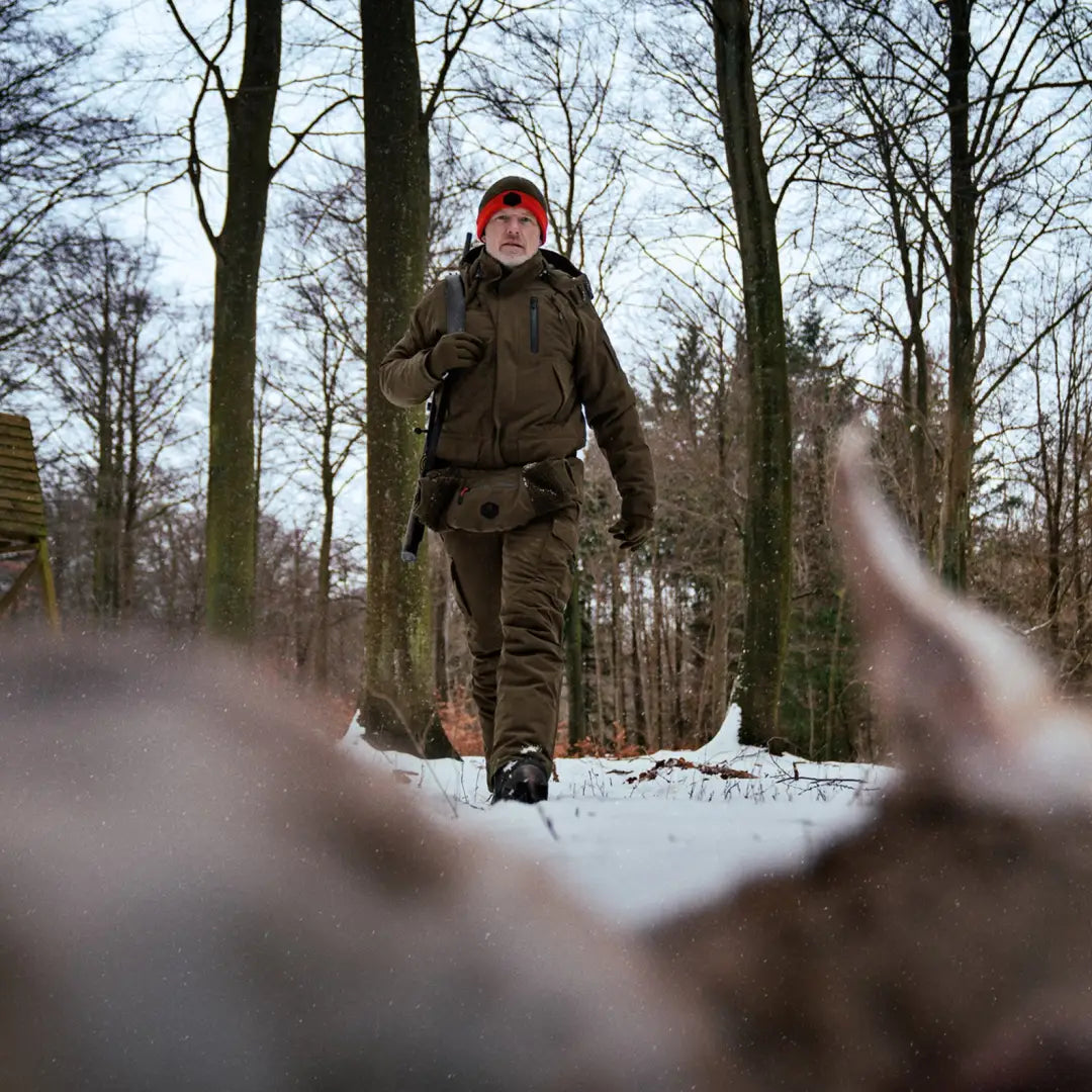 Person in winter gear and red hat in snowy forest wearing Harkila Driven Hunt HWS Insulated Jacket