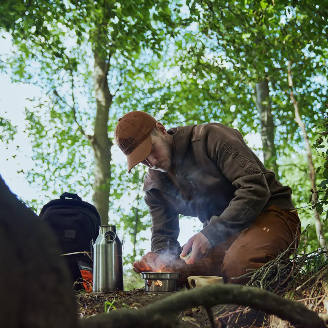 Person in Härkila Hoodie cooking over a fire in a cozy forest with zipped chest pocket