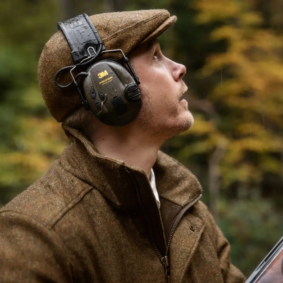 Person in hearing protection and a flat cap gazing up in Harkila Kenmore GTX Jacket