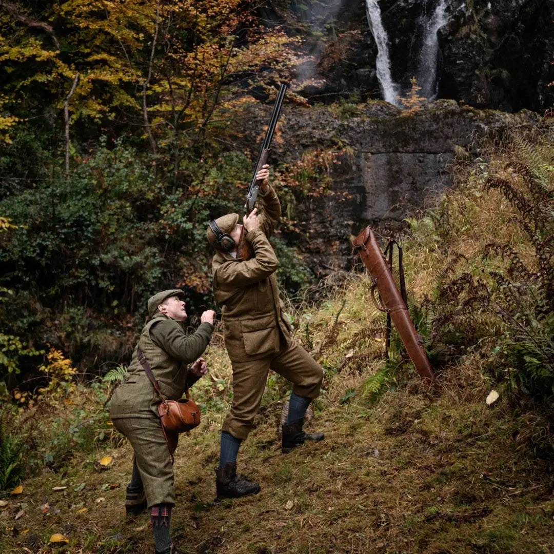 Two hunters in traditional attire aim rifles under trees, wearing Kenmore GTX Jacket