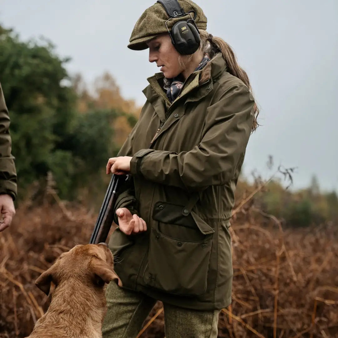 Hunter in protective gear with a shotgun and dog, showcasing Harkila Orton Tech HWS Jacket