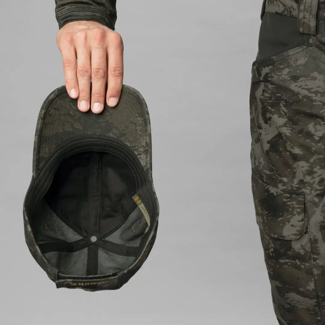 Hand holding a Harkila Modi Camo Cap showcasing military-style camouflage design