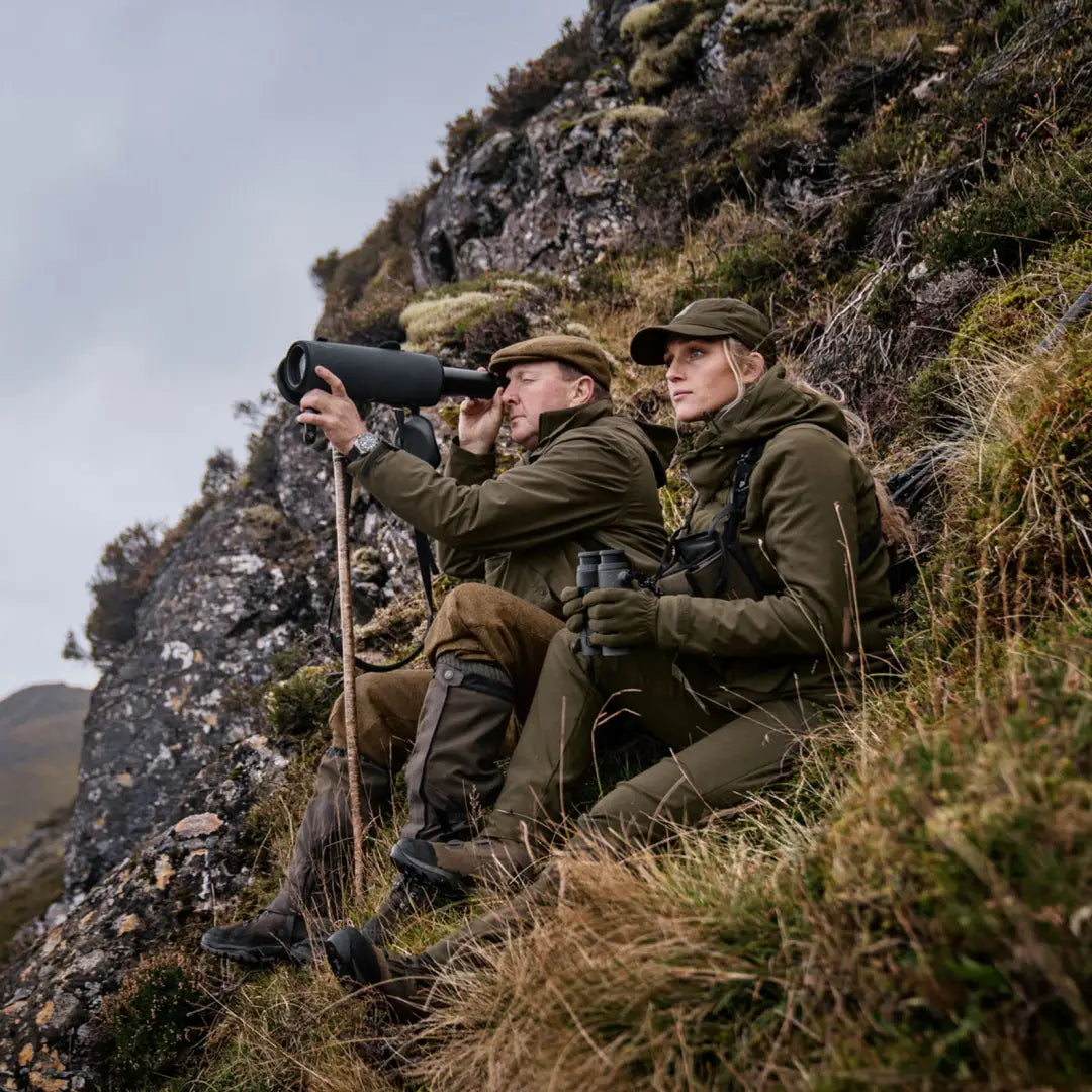 Two people in outdoor gear using a spotting scope on a rocky hillside with Harkila Pro Hunter GTX Ladies Jacket