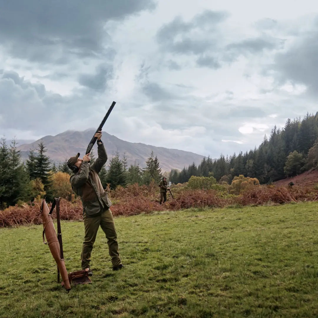 Hunter aiming shotgun in field, showcasing Harkila Rannoch HWS Shooting Jacket