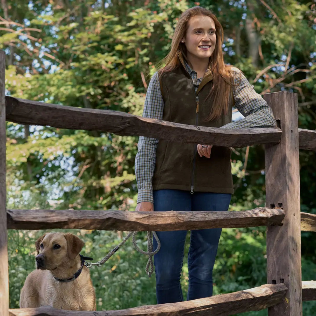 Woman in Harkila Sandhem Pro Women’s Waistcoat by a wooden fence with a dog