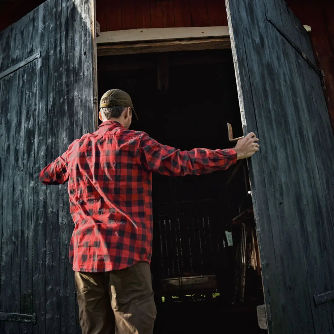 Person in a red plaid shirt opening barn doors, showcasing Harkila Scandinavian style