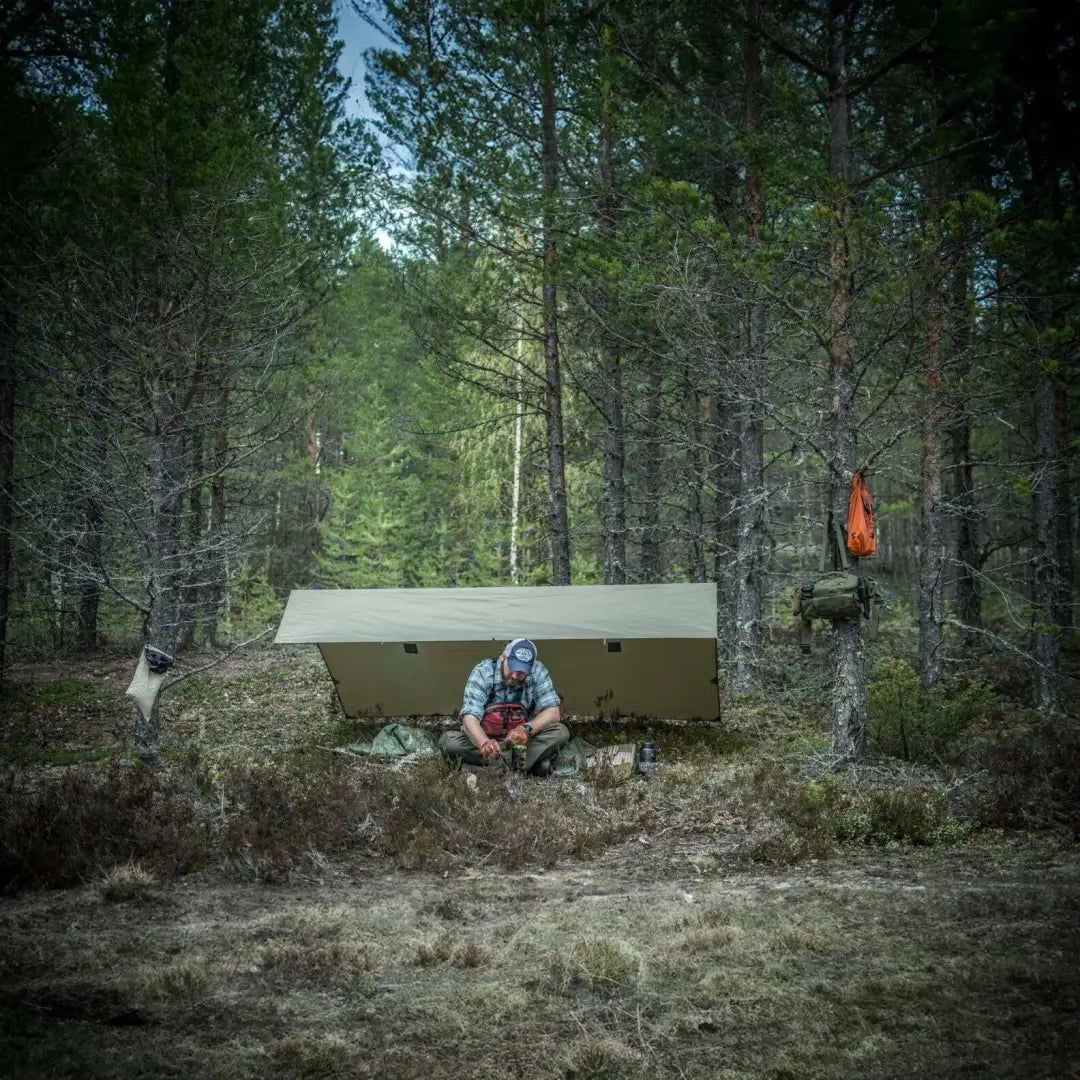 Person relaxing in a forest with Helikon-Tex Supertarp Small for impromptu shelter