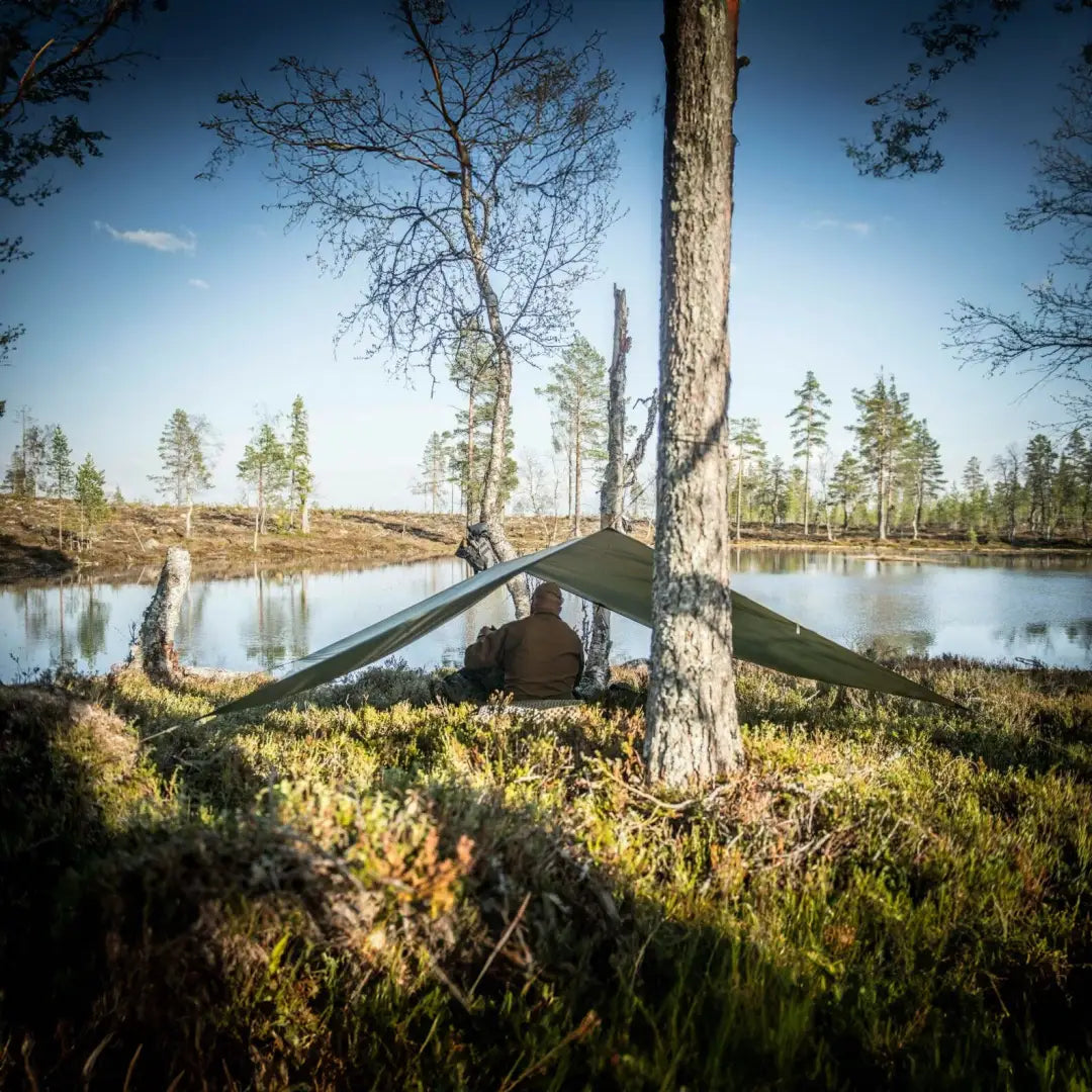 Tent between trees by a calm lake showcasing Helikon-Tex Supertarp Small for shelter