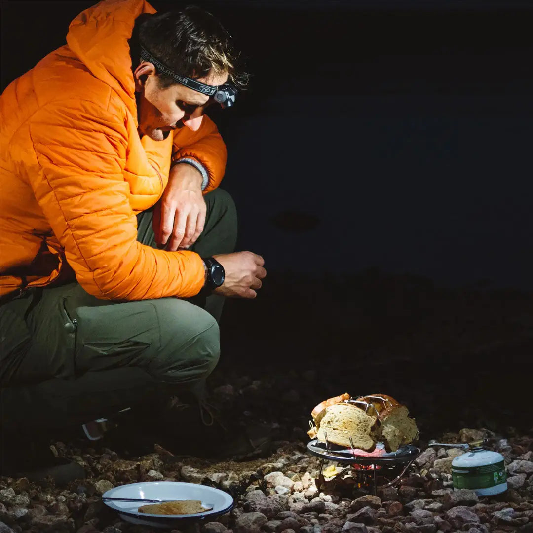 Person in a bright orange jacket using a Highlander slice camping toaster by cookware