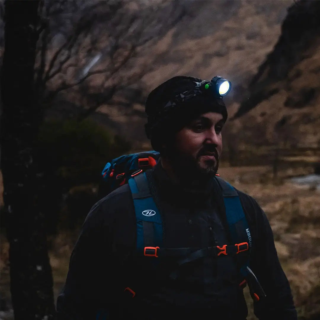 Bearded man with a Highlander Polaris Rechargeable head torch in a dark outdoor scene