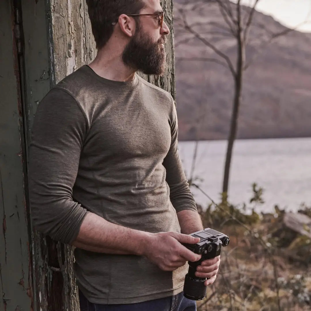 Bearded man in glasses wearing a crew neck merino wool base layer top while holding a camera