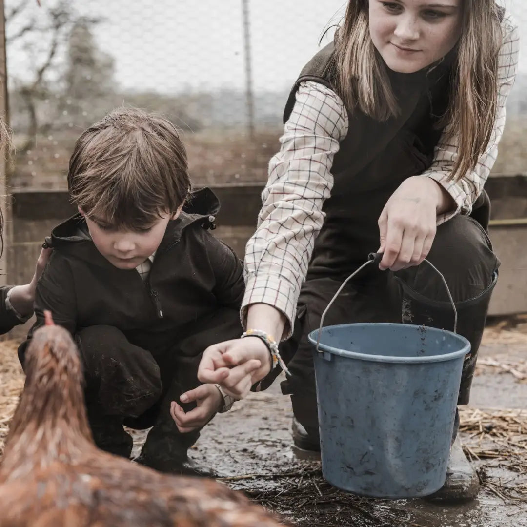 Kids in Hoggs Of Fife Ambassador Junior Tattersall Shirt feeding a chicken with a blue bucket