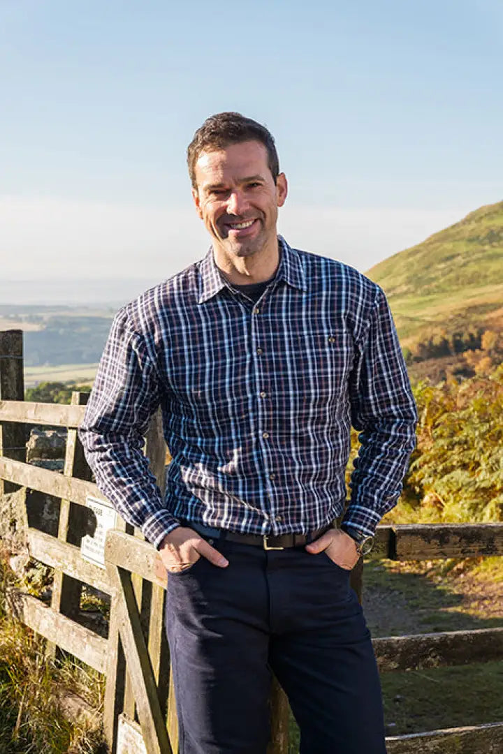 Smiling man in plaid shirt next to fence, showcasing Hoggs Of Fife Bark fleece lined shirt