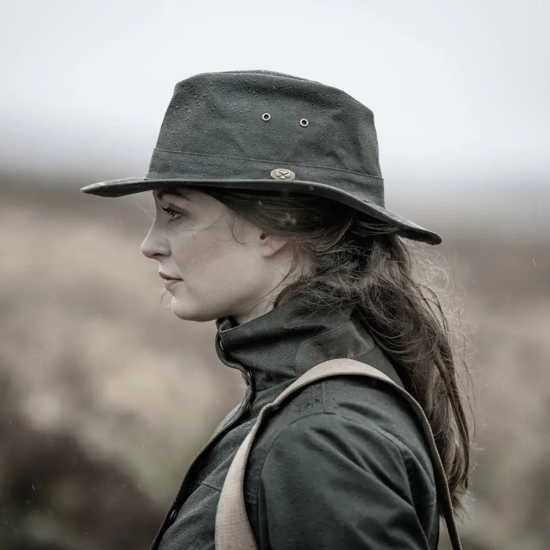 Dark green wide-brimmed hat on person with long hair, styled with Fife Caledonia Ladies Wax Jacket