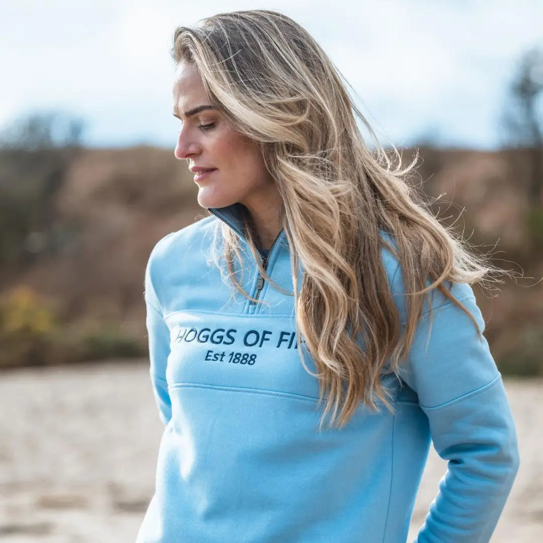 Woman with long blonde hair in a light blue ladies quarter zip sweatshirt from Hoggs of Fife