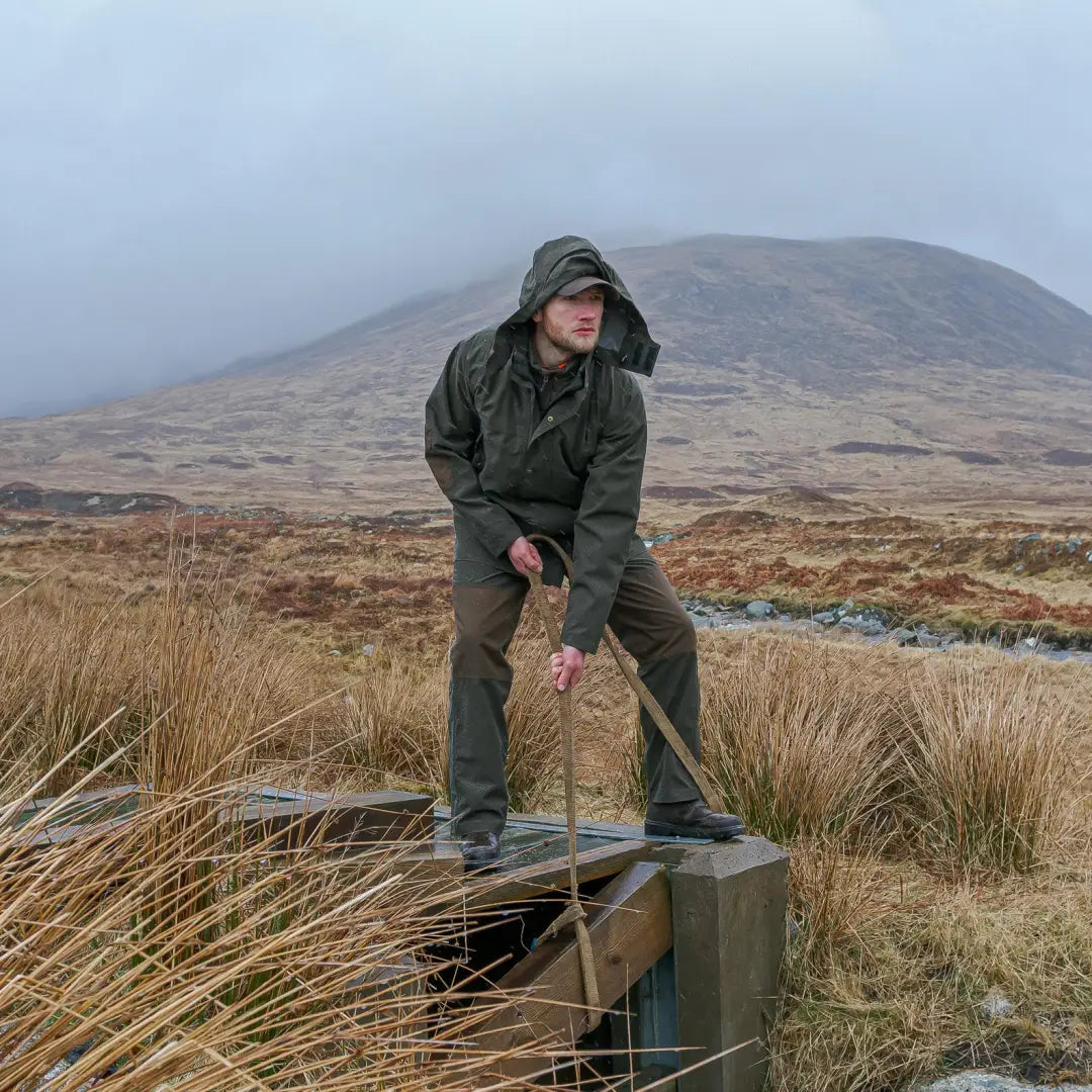 Person in Hoggs of Fife Green King II Waterproof Jacket on a wooden structure outdoors