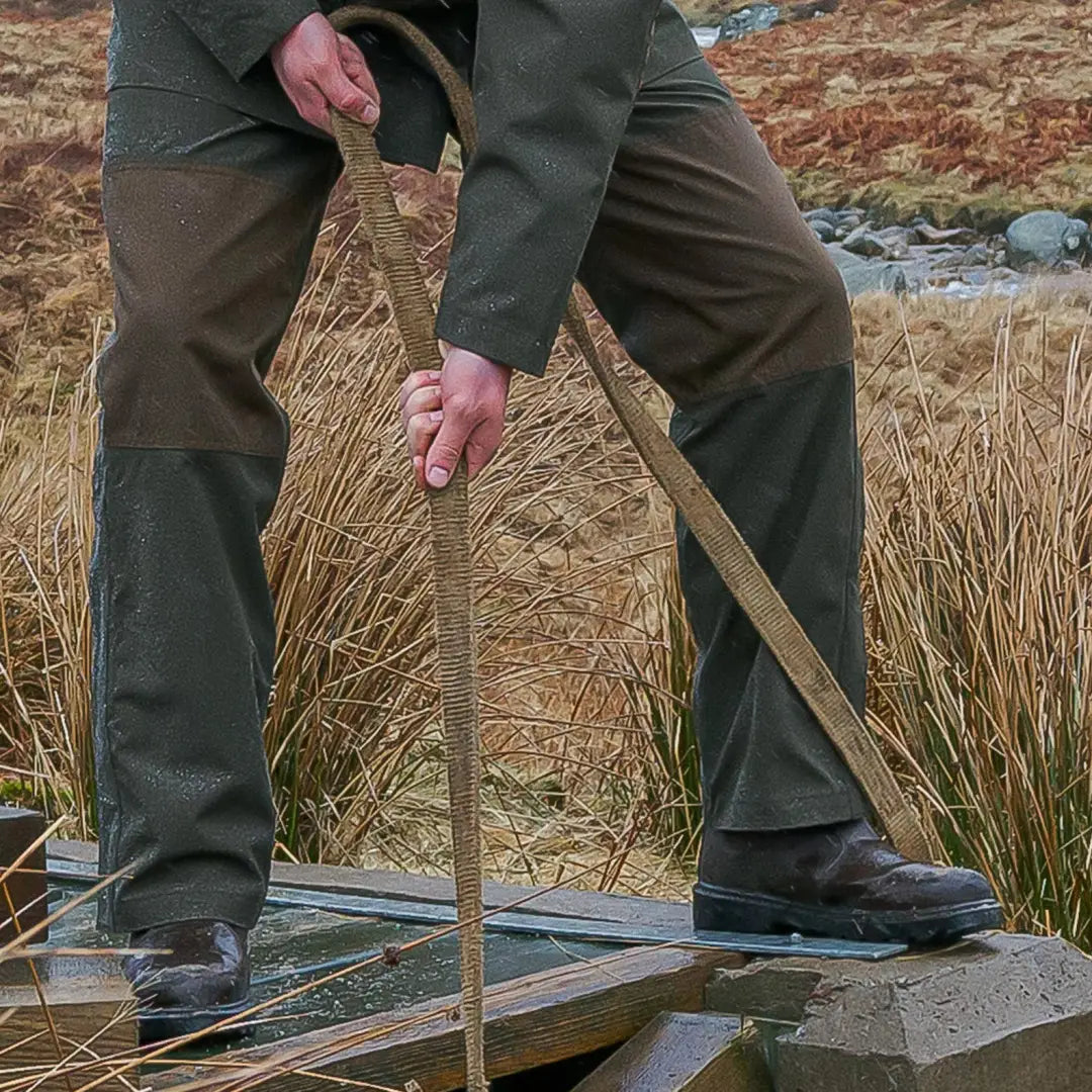 Person holding a wooden walking stick on a boardwalk wearing Fife Green King II Waterproof Trousers