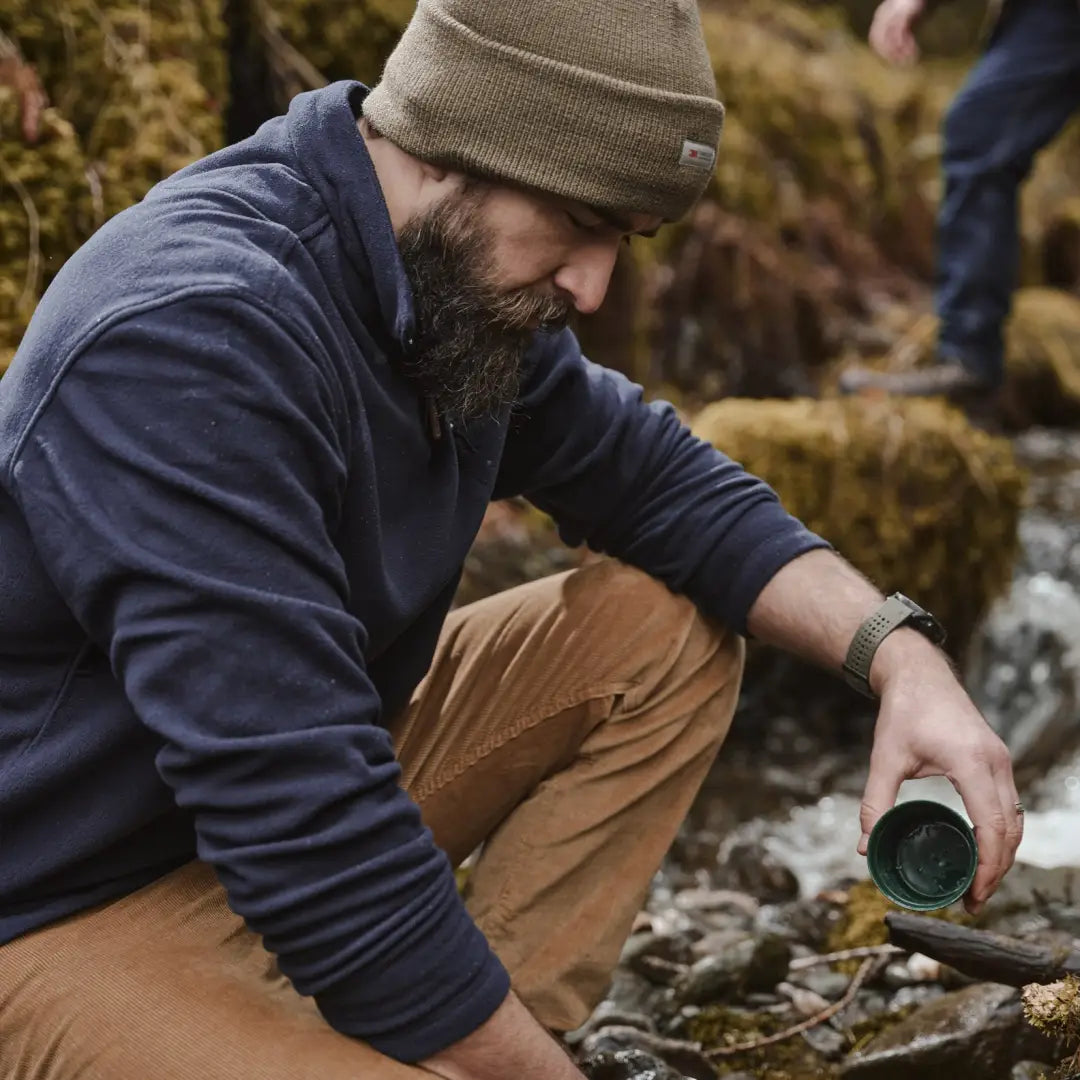 Bearded man in Hoggs of Fife Islander shirt by stream, showcasing country clothing for hunting