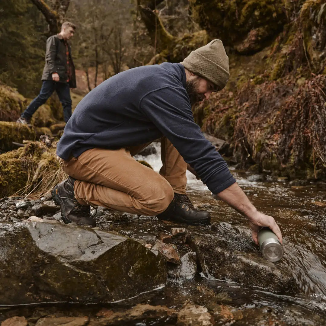 Person crouching on a rock filling a water bottle while wearing a Fife Islander shirt