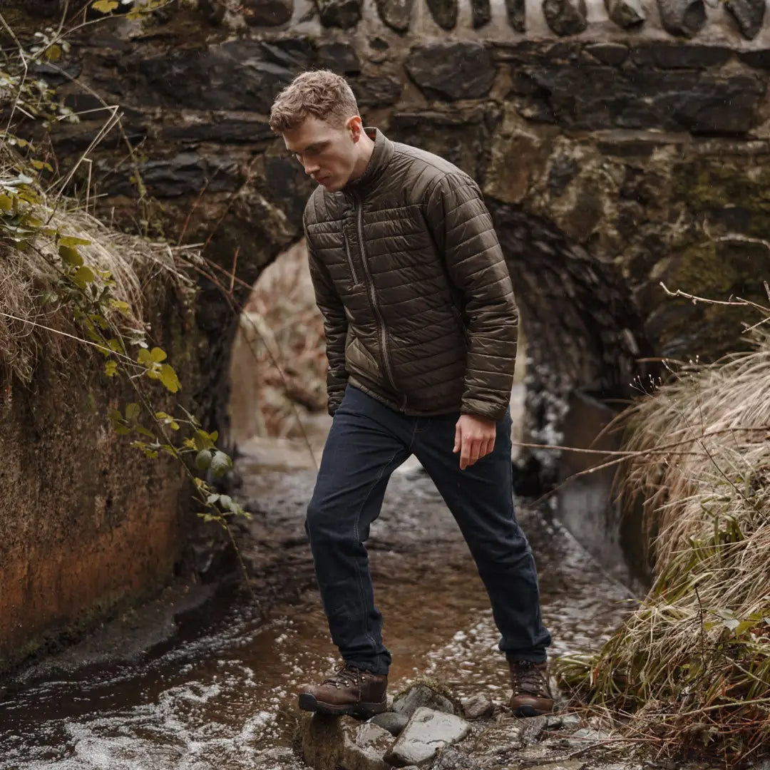 Man in brown Fife Kingston jacket stepping on rocks in a stream, perfect for country clothing