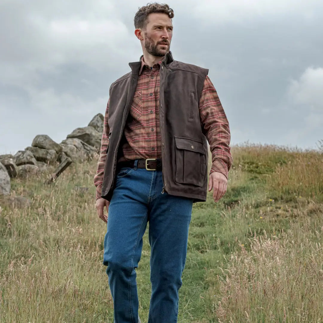 Man in brown Fife Lomond Leather Waistcoat, plaid shirt, and jeans in rural scene